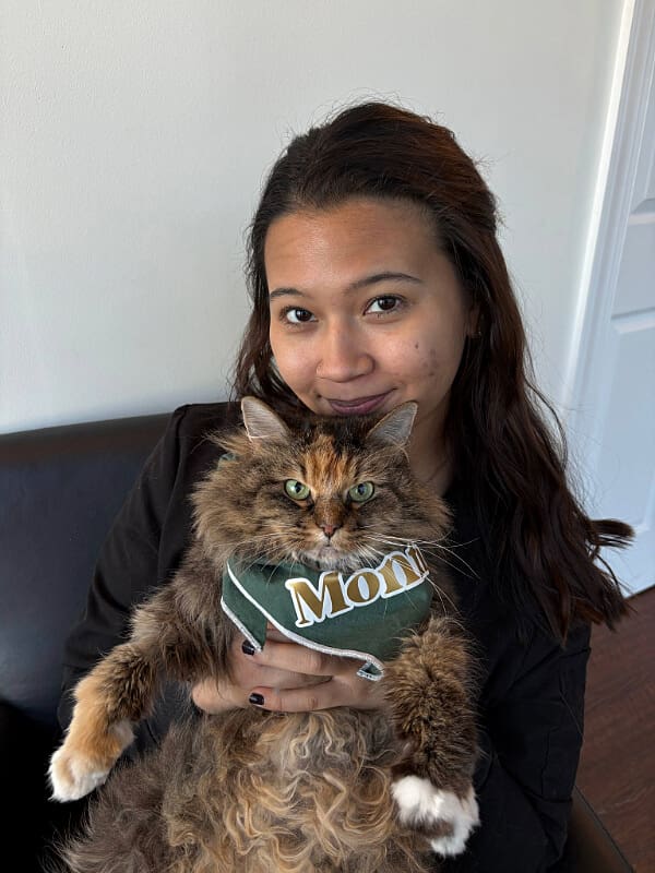 Female with long brown hair holding a stripped cat wearing a badanna